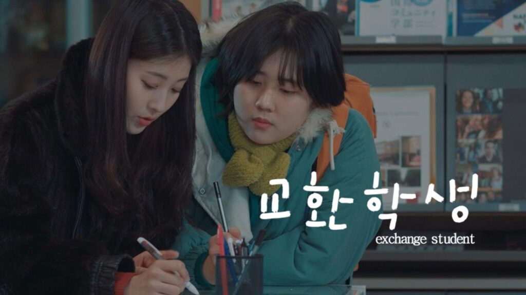 Film poster for “교환학생 | Exchange Student”, showing two women (actors both unlisted), wearing winter coats. One woman is filling out a form on high table, and the other is next to her, leaning over to look at what she’s writing.