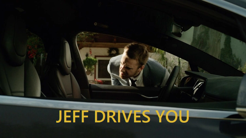 Image of the character David (Addison Heimann), dressed in a suit, looking through the driver’s seat window of a car that has no driver. The text JEFF DRIVES YOU is written in yellow over the image.