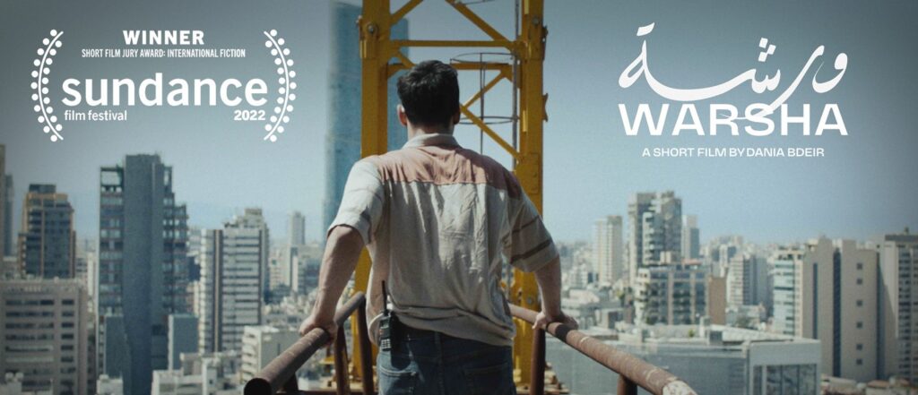 A man walks away from the camera on the bridge of a construction crane, with skyscrapers in the city in front of him. Text overlaid on the image says “Warsha: A short film by Dania Bdeir”, and also includes a laurel from the 2022 Sundance Film Festival for winning the short film jury award for international fiction.