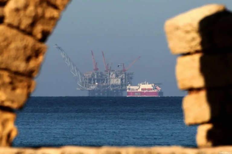 A giant gas rig with cranes and a docked ship are seen from the shore