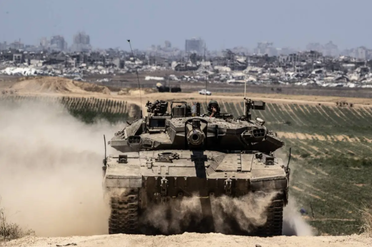 A tank in the foreground being driven towards the camera, while in the background is Gaza, with completely obliterated buildings all across the horizon.