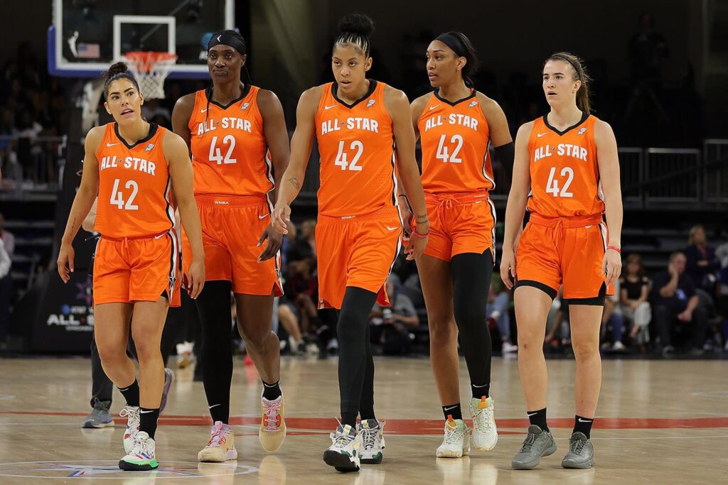 Five players walking on a basketball court in orange jerseys that all say "All-Star 42"