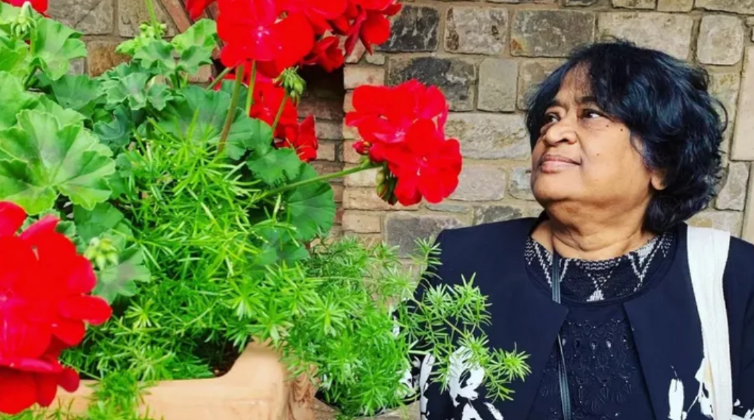 Photo of an Indian person with short black hair looking at a bush with large red flowers.